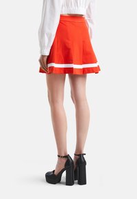 Röd utsvängd kjol med vita ränder i fållen, gjord av bomull. Matchad med svarta plattformsskor med ankelremmar.