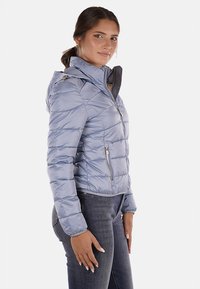 Giacca a vento blu chiaro con cappuccio, caratterizzata da una chiusura con zip e un motivo trapuntato diagonale. Tessuto liscio e lucido; vestibilità corta.