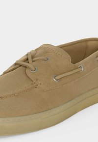 Ελαφρύ casual παπούτσι σκάφους από ταμπά σουέτ με λεπτομέρειες κορδονιών και μπεζ λαστιχένια σόλα, που δείχνει πλαϊνή και επάνω κοντινή όψη.