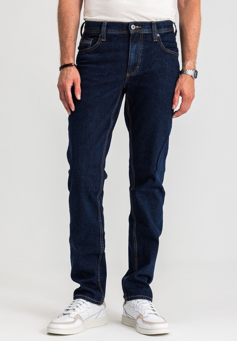 Ciemnoniebieskie dżinsy z denimu o prostym kroju nogawek, widoczne przeszycia ozdobne, fason z pięcioma kieszeniami oraz klasyczny pas z zapięciem na guzik.