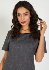 Top gris con mangas cortas, patrón geométrico texturizado y un acento negro en el cuello. La tela suave y el corte relajado aportan un detalle sutil.
