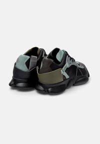 Sneaker nere e verdi con suola texturizzata nera, caratterizzate da materiali a strati in diverse tonalità e un design dei lacci unico.