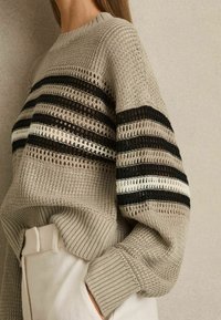 Szary dzianinowy sweter z poziomymi czarnymi, białymi i rudymi paskami; ma luźny krój i ściągacze, prezentując teksturowane otwarte sploty.