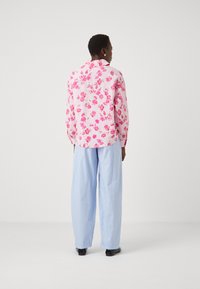 Blomstermønstret rosa skjorte med lange ermer, kombinert med lyseblå stripete vide bukser og svarte sko. Bakvinkel.