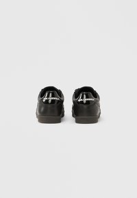 Schwarze Ledersneaker mit glatter Textur, mit einem glänzenden Absatz und weißem "KARL LAGERFELD"-Logo auf der Rückseite. Niedrig geschnittenes Design.