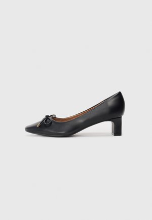Black leather pump with a pointed toe, small heel, and decorative bow detail on the front. Smooth texture and simple design.