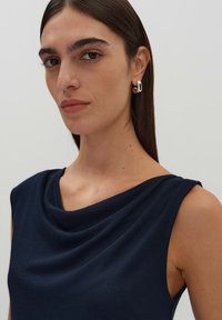 Top senza maniche blu navy con scollo drappeggiato, realizzato in un tessuto liscio. Orecchini a cerchio argentati completano il look.
