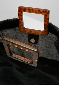 Svart fuskpälsväska med ett inre av fuskpäls och två fyrkantiga sköldpaddsformade handtag, varav ett är fäst vid en svart läderbotten med en metallisk tryckknappslåsning.