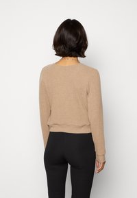 Beige ribbad stickad tröja med långa ärmar, rund halsringning och en åtsittande midja, bärs med svarta leggings. Slät textur, avslappnad design.