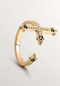 Anillo de metal dorado con un diseño abierto que presenta una forma de cruz acentuada con piedras negras y detalles de cuentas en los bordes.