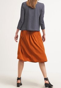 Striped navy long-sleeve top paired with a flowing orange midi skirt. Model wears chunky black heeled shoes. Smooth fabric and relaxed fit.