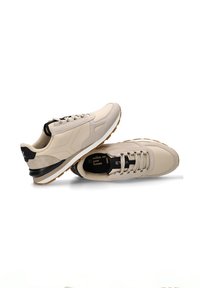 Zapatillas deportivas beige con parte superior de ante y cuero, que presentan una tapa de tacón negra, una media suela blanca y una suela exterior de goma texturizada. Diseño neutro.