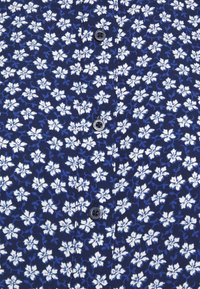 Marinblå skjorta med ett vitt blommönster, med blå accenter och svarta knappar framtill. Lätthanterligt tyg med en slät yta.