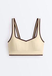 Brassière de sport beige avec double fines bretelles et bordure marron le long des bords, conçue pour un soutien léger et un confort optimal.