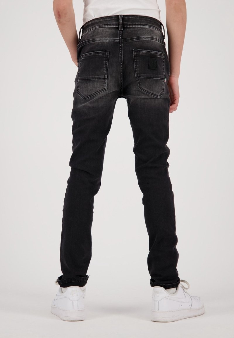 Jean skinny noir avec un lavage délavé, doté de deux poches arrière et d'un patch de logo. Assorti à des baskets blanches, montrant un look décontracté.