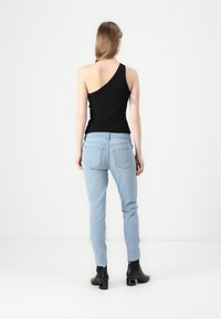 Top negro de un solo hombro combinado con jeans ajustados de un azul claro, que cuentan con un diseño clásico de cinco bolsillos y botas de tobillo negras con tacón.