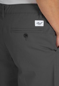 Gray shorts made of smooth fabric, featuring a rear pocket with a button and a white branded label stitched above it.