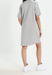 Robe t-shirt oversized grise en coton doux, avec des manches courtes et un ourlet arrondi, accompagnée de baskets de sport blanches.