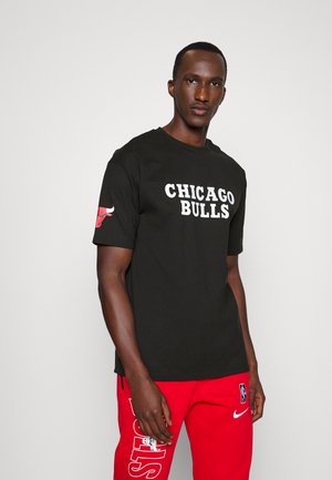 Camiseta negra de manga corta con el texto "CHICAGO BULLS" en blanco y un logo de toro rojo en la manga izquierda, combinada con joggers rojos.