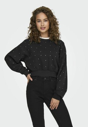 Felpa nera con borchie argentate, design cropped, maniche oversized, polsini a coste, abbinata a jeans neri a vita alta.
