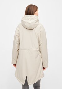 Beige waterproof parka with a hood, features a cinched waist, long sleeves, and a curved hem with a small vent at the back.