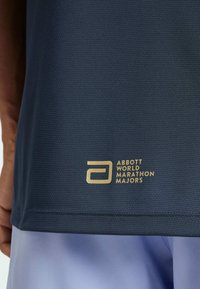 Navy blue athletic shirt with textured fabric, featuring a gold logo reading "Abbott World Marathon Majors" near the hem.