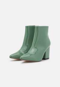 Botas de tobillo de charol verde con punta afilada y tacón alto grueso. Cuentan con un cierre de cremallera y un acabado suave y brillante.
