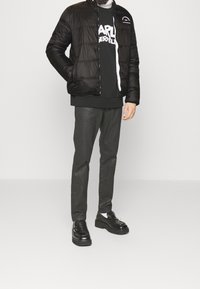 Svart pufferjacka med quiltad design, bärs över en svart sweatshirt med vit text, i kombination med mörka byxor och svarta plattformsskor.