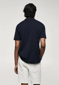 T-paita lyhyillä hihoilla, tummansininen, pehmeää kangasta, yhdistettynä vaaleisiin shortsihousuihin, nähtynä takaa. Yksinkertainen muotoilu ilman näkyviä kuvioita.