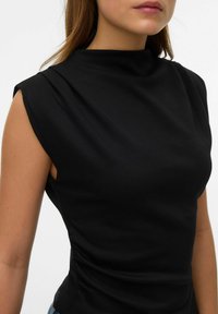 Sort ærmeløs top lavet af elastisk materiale, med høj halsudskæring og side-rynkedetalje for et tætsiddende look.