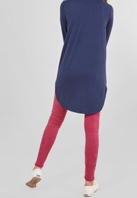 Haut long bleu marine avec un ourlet arrondi associé à des leggings roses. Les chaussures sont blanches avec une semelle texturée. Affiché de dos.