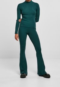 Teal geribbelde gebreide set met een lange mouwen coltrui en flared broeken, aangevuld met chunky zwarte plateau schoenen.