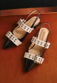 Scarpe slingback con punta a punta, finitura nera lucida, cinturini bianchi a contrasto con occhielli e dettagli con fibbie argento.