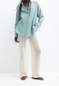Chemise en lin bleu clair à manches longues avec fermeture à boutons, associée à un pantalon en crochet crème, ample, avec une taille à cordon.