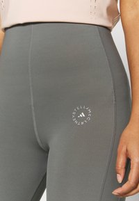 Szare legginsy z wysokim stanem, wykonane z elastycznego materiału, z okrągłym białym logo na udzie oraz płaskimi szwami dla komfortu.