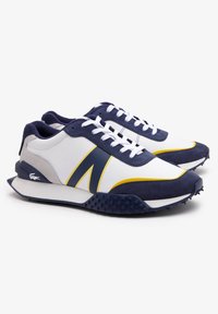 Zapatos deportivos para hombres con una parte superior de cuero blanco, detalles en gamuza azul marino, acentos amarillos y una suela de goma texturizada con picos.