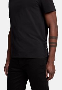Maglietta nera in cotone con maniche corte, scollatura a girocollo e un sottile spacco laterale. Abbinata a jeans neri. Design semplice senza motivi o dettagli.