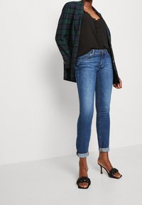 Černý top s krajkovým lemem pod zeleno-námořnickým kostkovaným sako, spárovaný s světle modrými slim džíny a černými sandály na podpatku s tkaným popruhem.