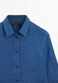 Blue long-sleeve shirt with collar and front buttons, made of textured fabric, displayed on a white background.