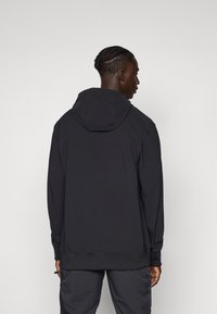 Zwarte hoodie met lange mouwen, gemaakt van een glad materiaal, met een relaxte pasvorm en ribbelboorden aan de mouwen en onderkant. Achteraanzicht getoond.