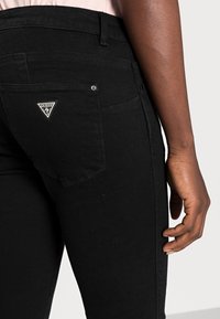 Jeans de mezclilla negra con un diseño ajustado, que presentan un bolsillo trasero con un logo triangular, costuras visibles y una cintura de altura media.