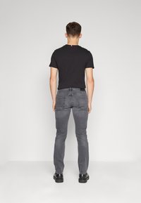 Camiseta negra de cuello redondo, vaqueros gris ajustados y botas negras. El conjunto presenta un diseño casual con una textura suave y detalles clásicos.