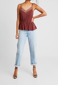 Bordó peplum top s krajkovým lemem a nastavitelnými špagetovými ramínky, spárovaný se světle modrými džínami s ohrnutými manžetami a černými sandály na podpatku.