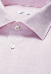 Chemise en lin rose clair avec col classique, deux boutons blancs attachés, et étiquette de marque "seidensticker" visible à l'intérieur du col.