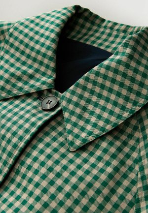 Kariertes grünes und beiges Stoffmaterial mit Kragen und einem dunklen Knopf, samtiger Textur. Nahaufnahme der Design-Details.