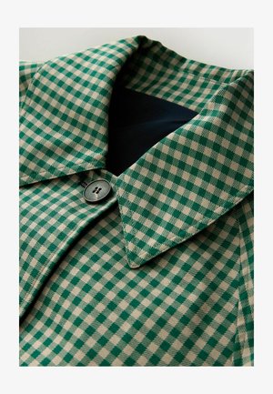 Ruuduline roheline ja beež kangas, millel on kraega kaelus, tume nupp ja sile tekstuur. Lähedalt vaadeldes disaini detailid.