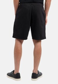 Zwarte katoenen sweatshorts met een elastische tailleband, zijzakken en een losse pasvorm, gecombineerd met zwarte sneakers met een witte zool.