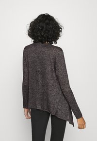 Tmavě mahagonový pletený svetr s dlouhými rukávy, asymetrickým lemem, strukturovanou látkou a volným střihem. Detaily zahrnují kulatý výstřih.