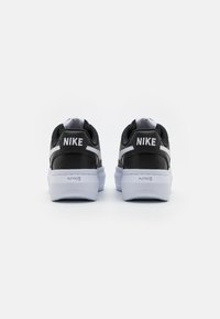 Svarta Nike-sneakers med en texturerad ovandel, vita accenter och vadderad krage. Har "Nike"-logotypen på hälen och en kontrasterande vit sula.