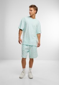 Mintgrønn teksturert kortermet skjorte og matchende shorts, med et preget mønster, kombinert med hvite joggesko og ankelsokker.